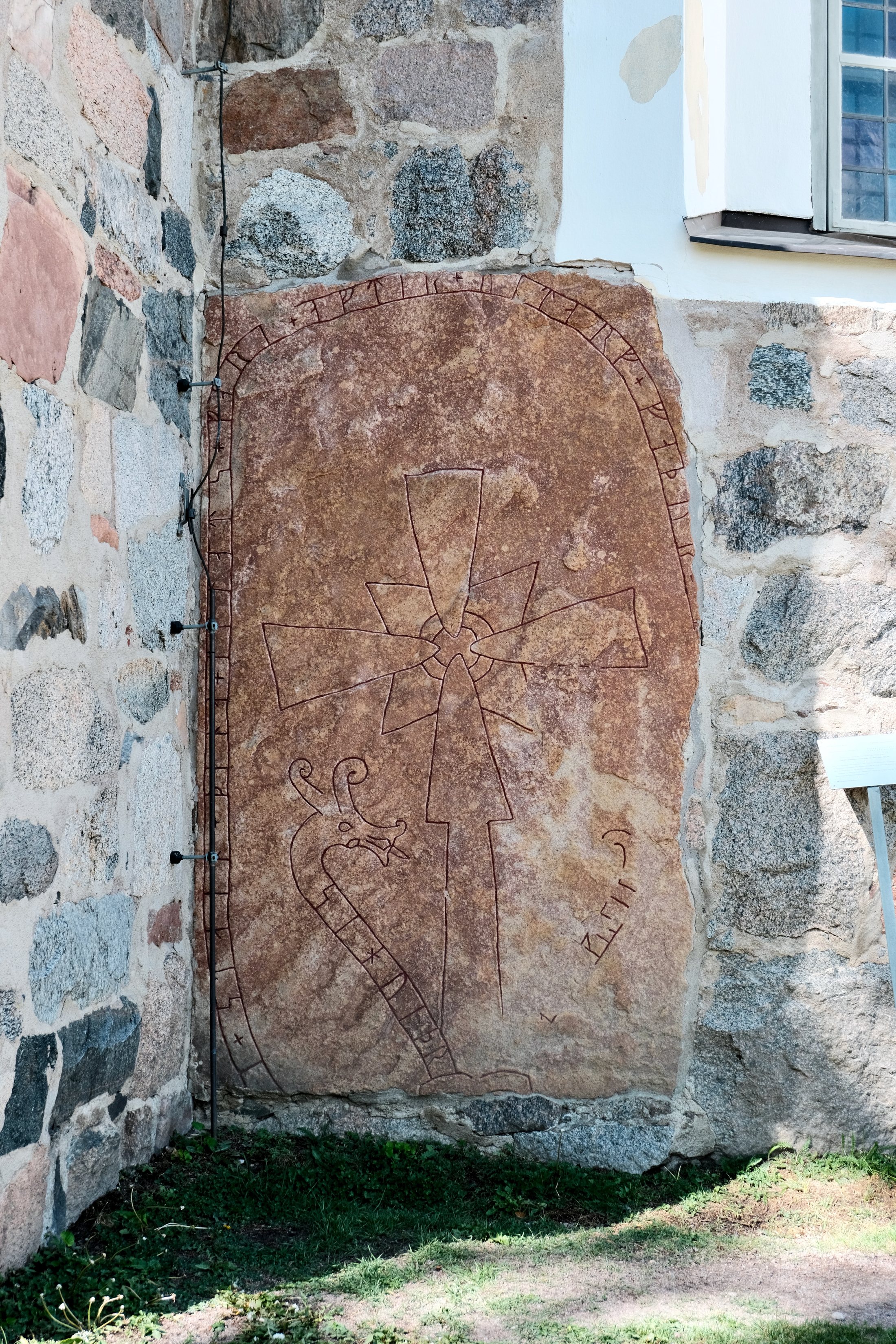 Runestone U 978 built into the wall of the Church of Old Uppsala in Sweden, showing a carved cross, runic inscription, and weathered stone surface.