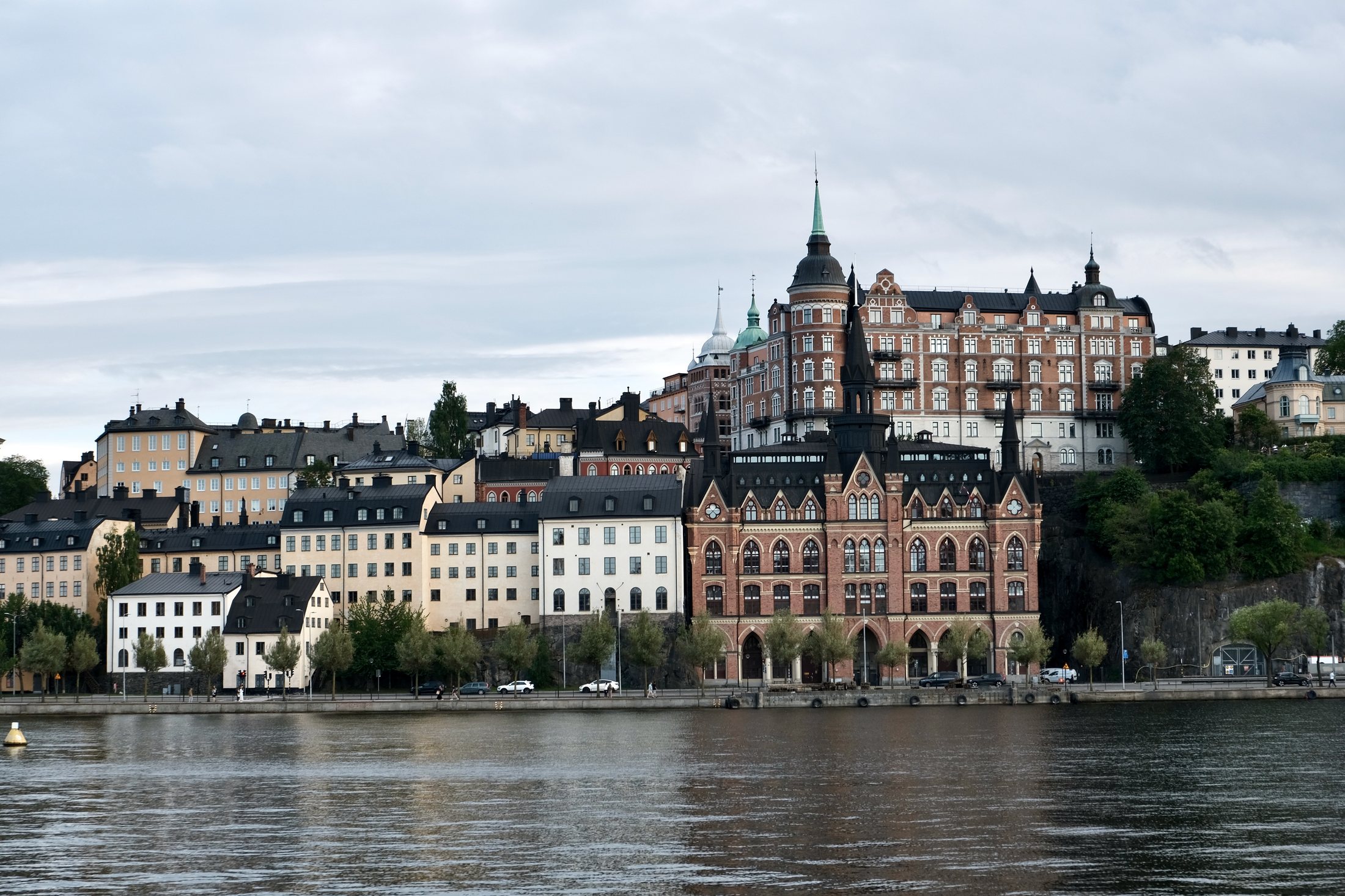 A waterfront view from Södra Riddarholmshamnen in Stockholm, looking across the water toward Söder Mälarstrand and Mariahissen, with historic buildings rising above the shoreline.