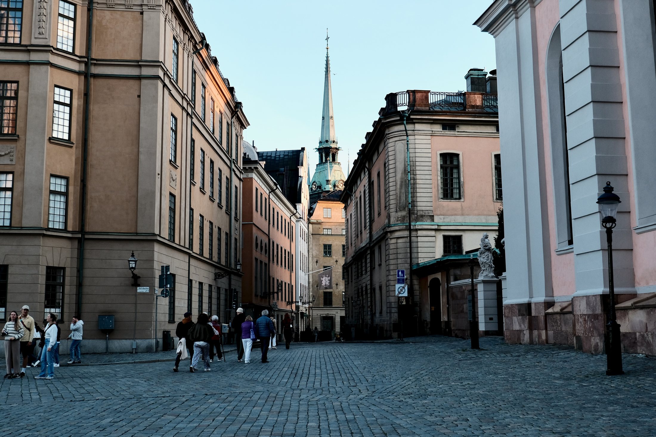 A cobblestone street in Gamla Stan, Stockholm, leading toward the tower of the German Church between historic buildings.