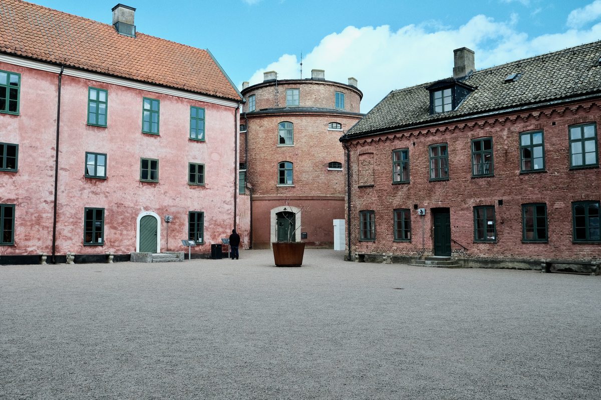 The inner courtyard of Landskrona Slott in Sweden, with pink and red brick historic buildings, green-framed windows, and a single person standing near the center.