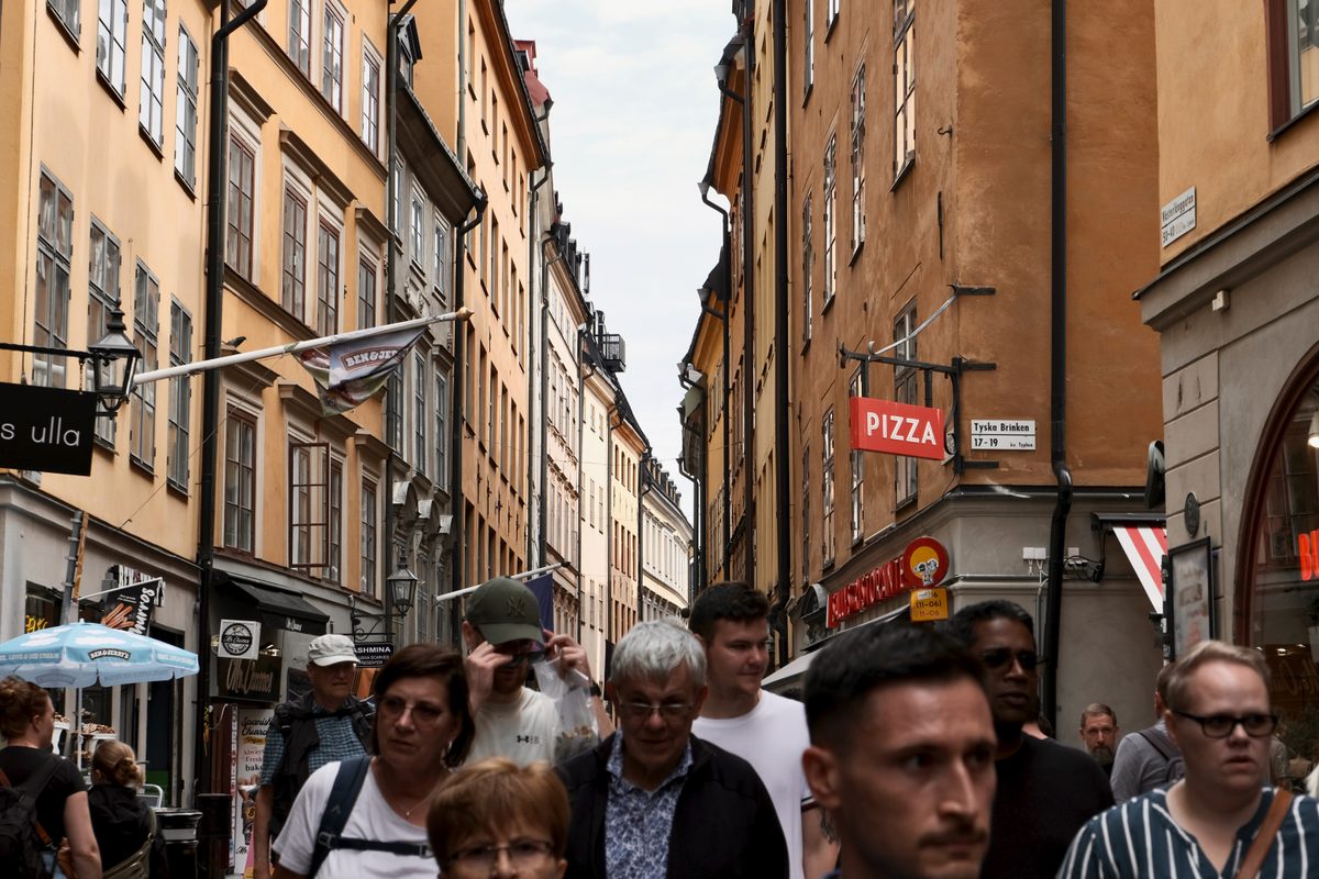 A crowded street in Gamla Stan, Stockholm, with people walking between historic buildings, shop signs, restaurants, and narrow old-town façades.