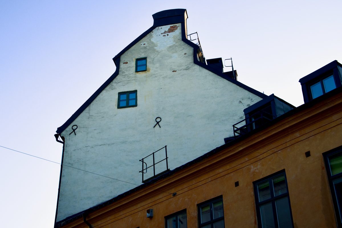 An upward view of an old building façade in Gamla Stan, Stockholm, with a pale gabled wall, small windows, and warm-toned historic architecture below.