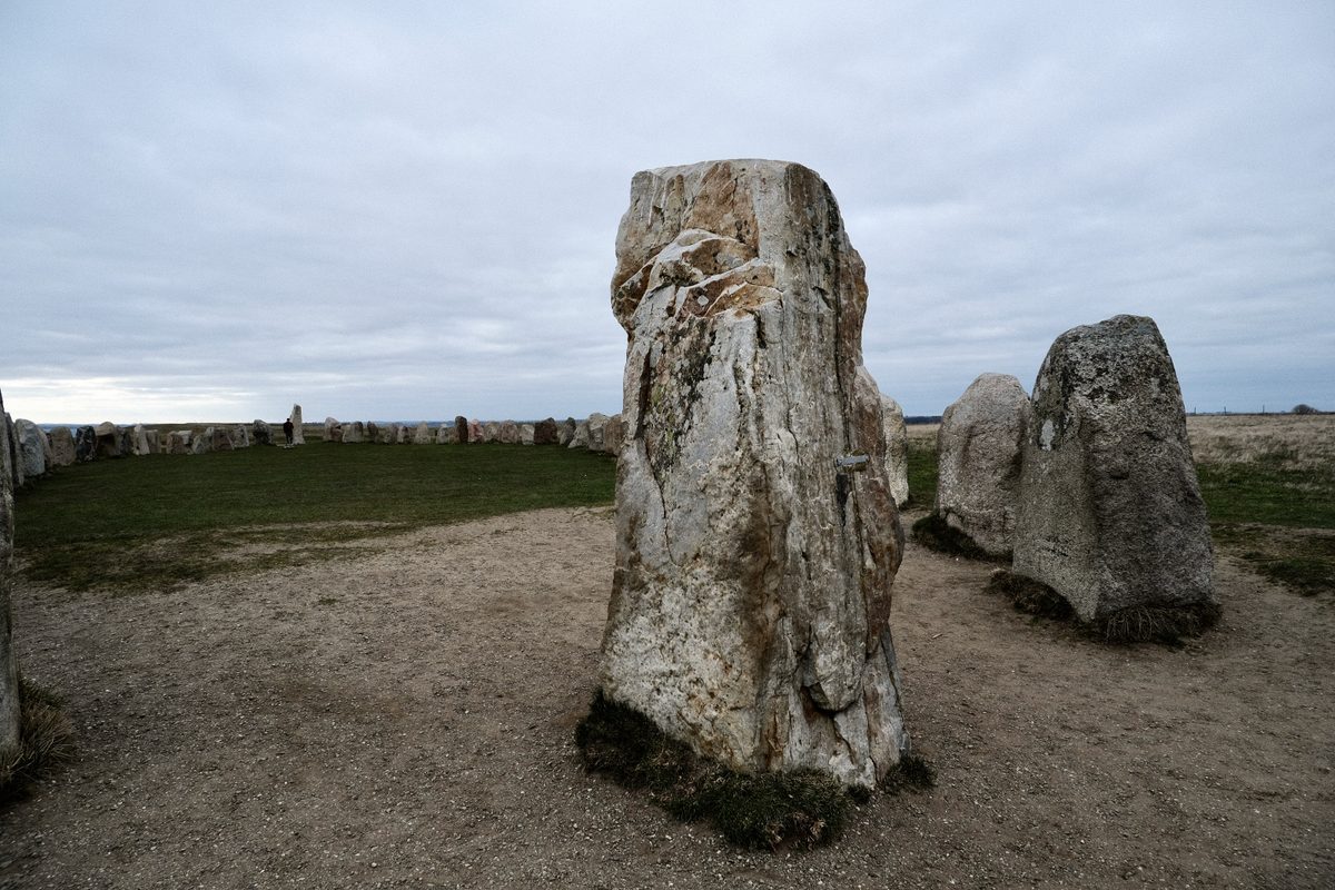 A close view of a large standing stone at Ales Stenar in Kåseberga, Sweden, with other stones forming a ship-shaped monument under a grey cloudy sky.