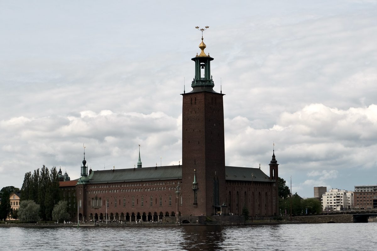 Stockholm City Hall seen from across the water, with its tall brick tower rising under a cloudy sky.