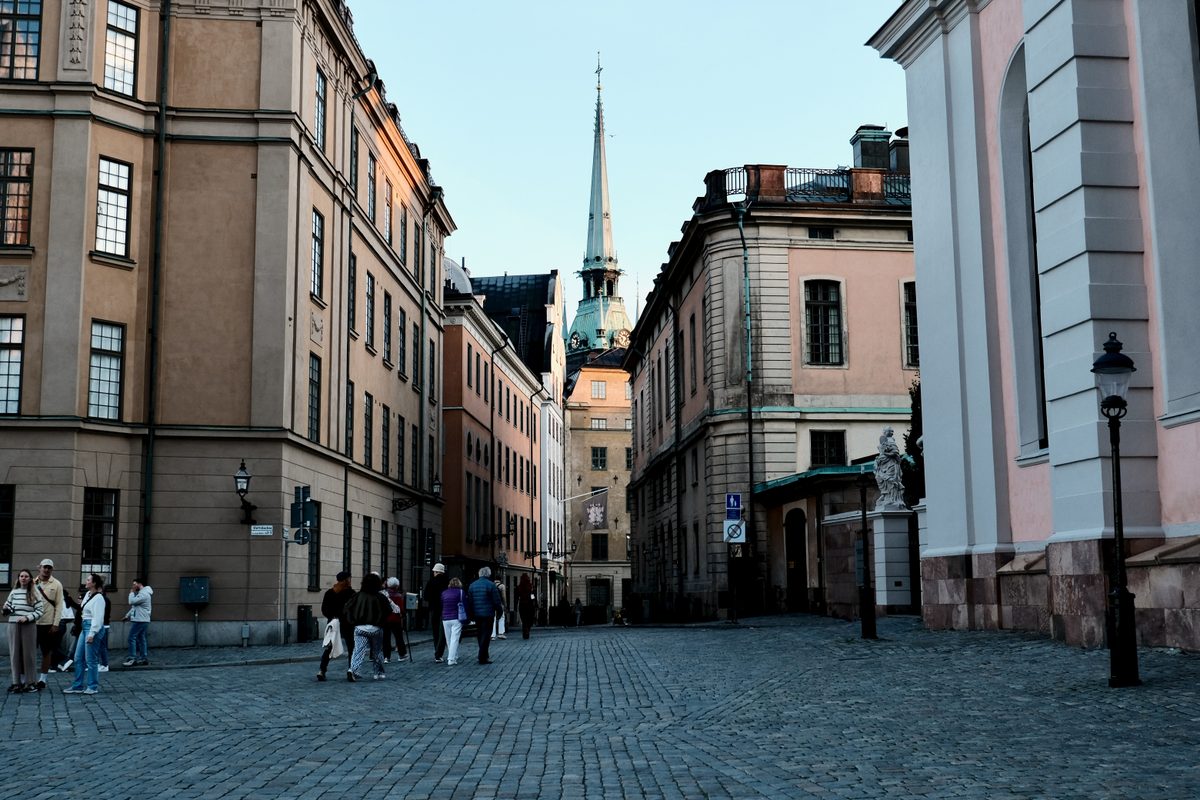 A cobblestone street in Gamla Stan, Stockholm, leading toward the tower of the German Church between historic buildings.