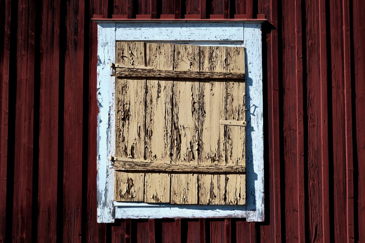 A close view of a weathered yellow wooden window shutter set into a red wooden building at Lövånger Kyrkstad in Västerbotten, Sweden.